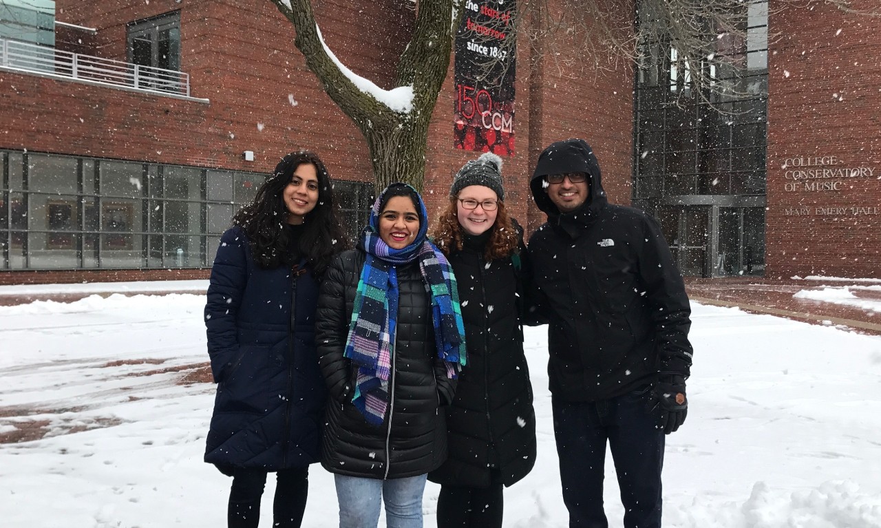 A group of students stands in the snow outside of the College-Conservatory of Music.